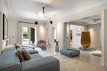 A bright, modern living room featuring a large light-blue sectional sofa, neutral tones, and elegant statement furniture.