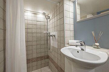 A clean bathroom featuring a tiled shower stall with a white curtain next to a pedestal sink, mirror, and light blue wall.