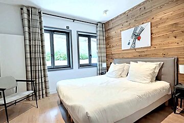 A cozy, modern bedroom with a large white bed, wood accent wall, ski lift art, and windows with plaid curtains.