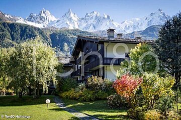A house with mountains in the background is surrounded by trees