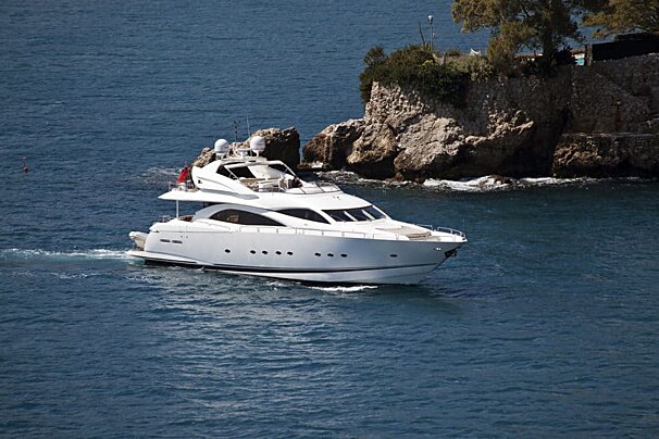 A white yacht is floating in the ocean near a rocky cliff