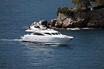 A white yacht is floating in the ocean near a rocky cliff