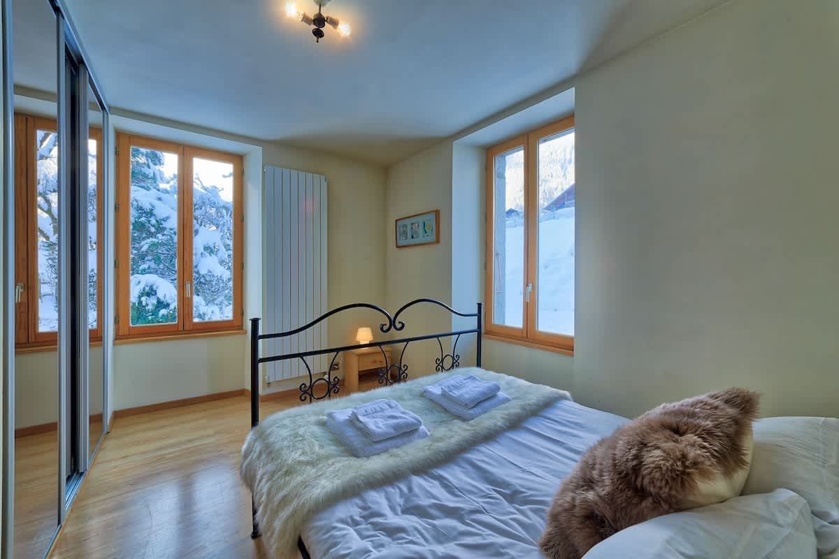 Cozy cabin bedroom featuring a wrought-iron bed with snowy views through large wooden-framed windows.
