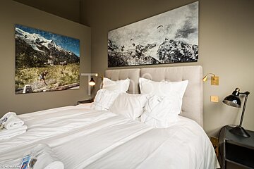 A bedroom with a large painting of a mountain on the wall above the bed