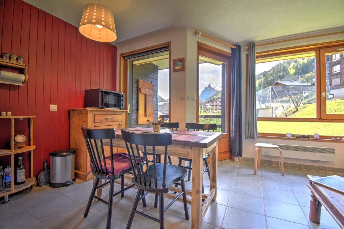 A rustic dining area with a red paneled wall, wooden table, and large windows showcasing a scenic mountain and green landscape view.