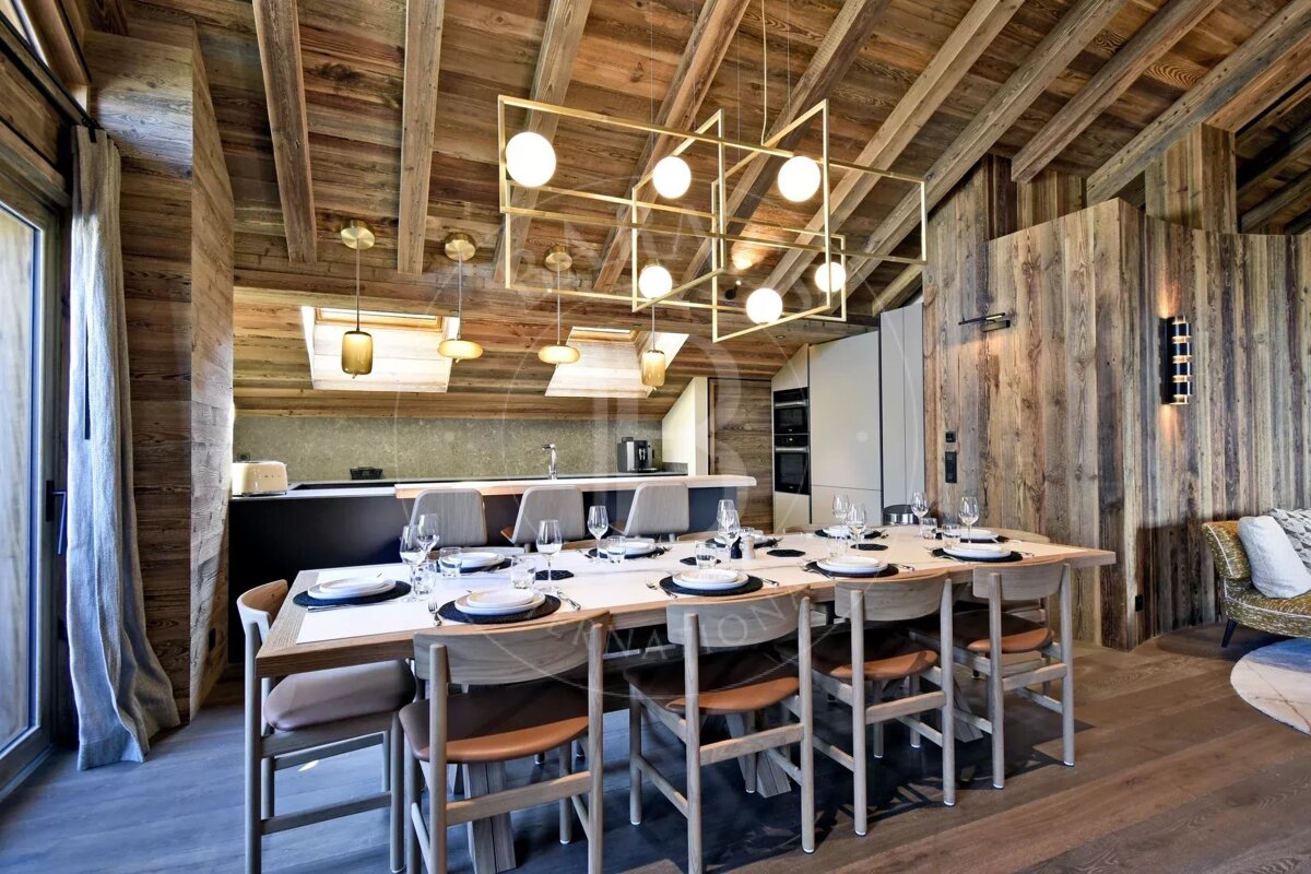 Rustic wooden dining room featuring a long table set for a meal, a modern brass chandelier, and exposed wood ceilings and walls.