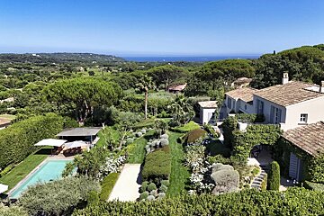 Luxurious Mediterranean-style villa with a swimming pool, lush gardens, and scenic ocean views under a clear blue sky.