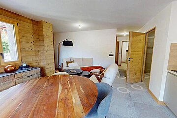 A modern living and dining area features wood paneling, a round wooden table, a light sofa with an orange throw, and a stylish floor lamp.
