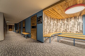 Modern ski lodge interior with blue walls, wood lockers, benches, and a distinctive ski-patterned wall under a warm wooden ceiling.