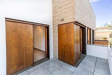 Modern terrace with grey tiled flooring, stone walls, and large wooden sliding doors that open to an empty interior room.