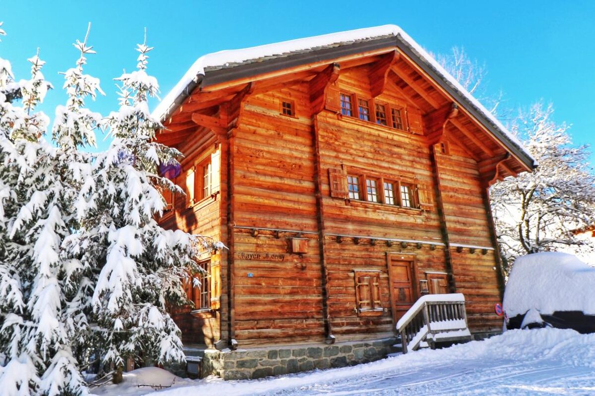 A large log cabin is surrounded by snow covered trees