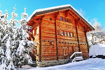 A large log cabin is surrounded by snow covered trees