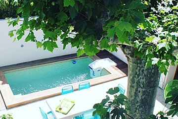 A small swimming pool is surrounded by a tree and a table and chairs