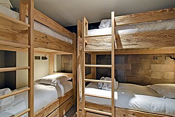 A modern bunk bed room with multiple wooden beds and crisp white bedding. Features include ladders, pillows, and cozy lighting.
