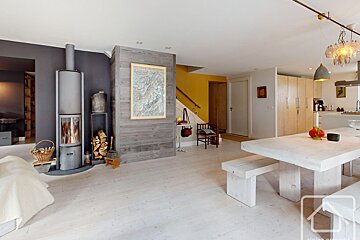 A modern, rustic open-plan living room and dining area with a wood-burning stove and light wood floors.