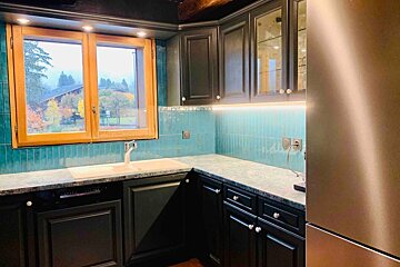 A kitchen with black cabinets and a stainless steel refrigerator