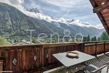 A table with a bowl on it sits on a balcony with mountains in the background