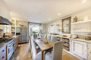 A spacious kitchen with a long wooden dining table, white chairs, and elegant rustic cabinetry.