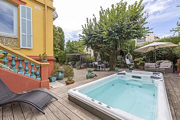 Vibrant yellow and orange house with a lush garden, featuring a hot tub on a wooden deck, outdoor dining, and lounging areas under trees.