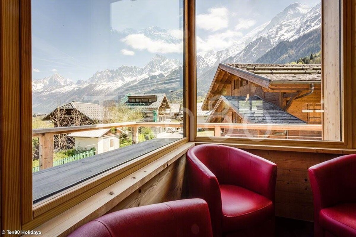 Two red chairs in front of a window with mountains in the background