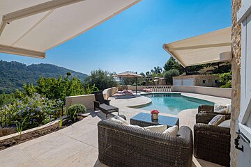 A large swimming pool is surrounded by patio furniture and an awning