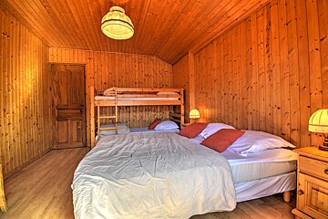 A cozy cabin bedroom featuring wood-paneled walls, a large bed with red pillows, and a wooden bunk bed.