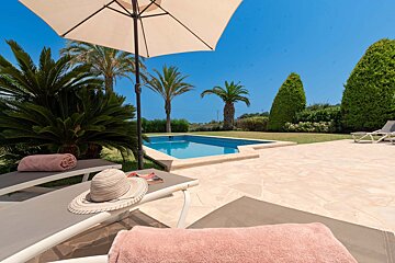 A lawn chair with a hat and a towel on it in front of a swimming pool