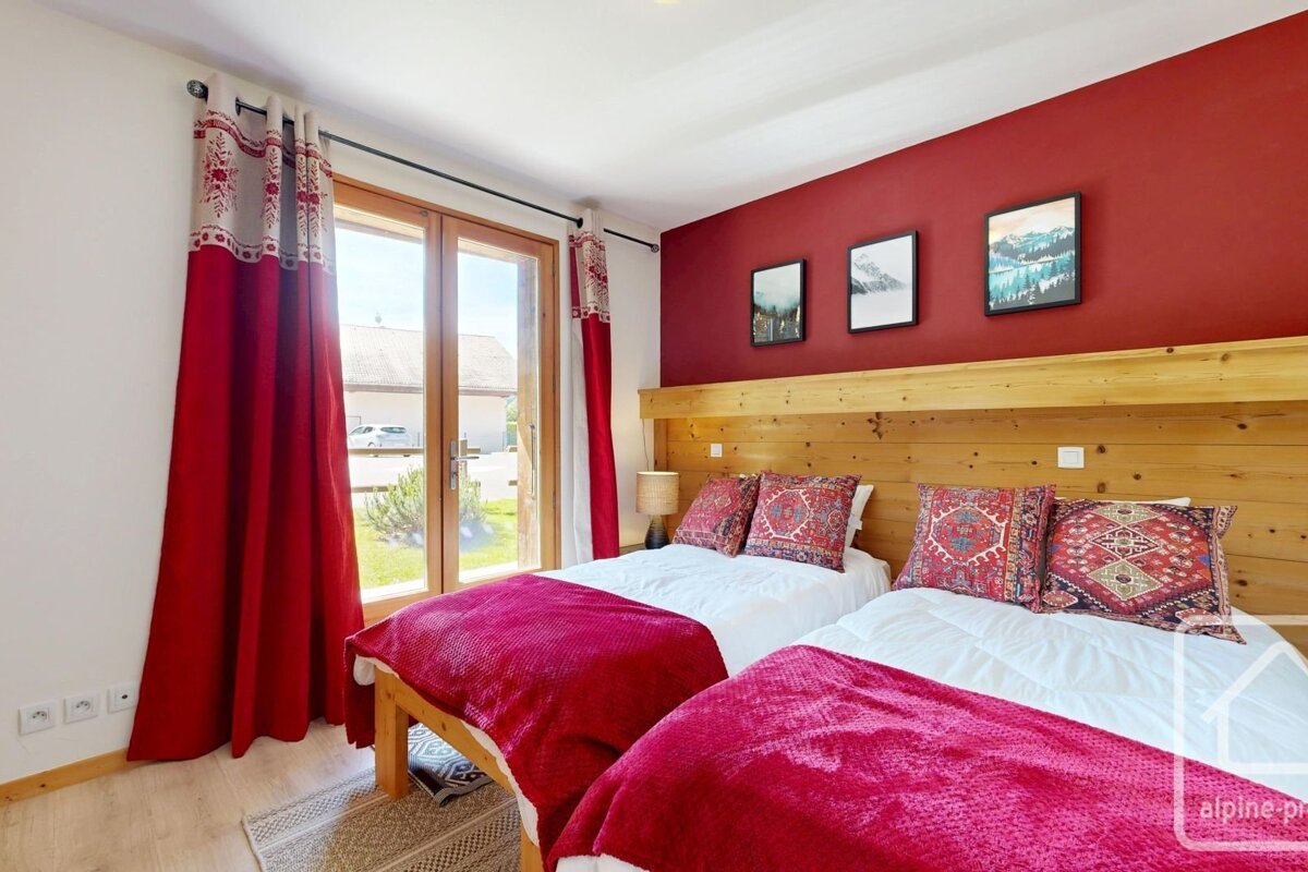 A bedroom featuring two twin beds with red throws, wooden headboards, red accent wall, and patio doors.