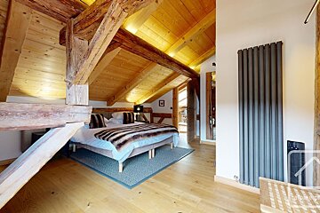 Rustic attic bedroom featuring exposed wooden beams, a sloped wooden ceiling, cozy bed, and a modern grey radiator.