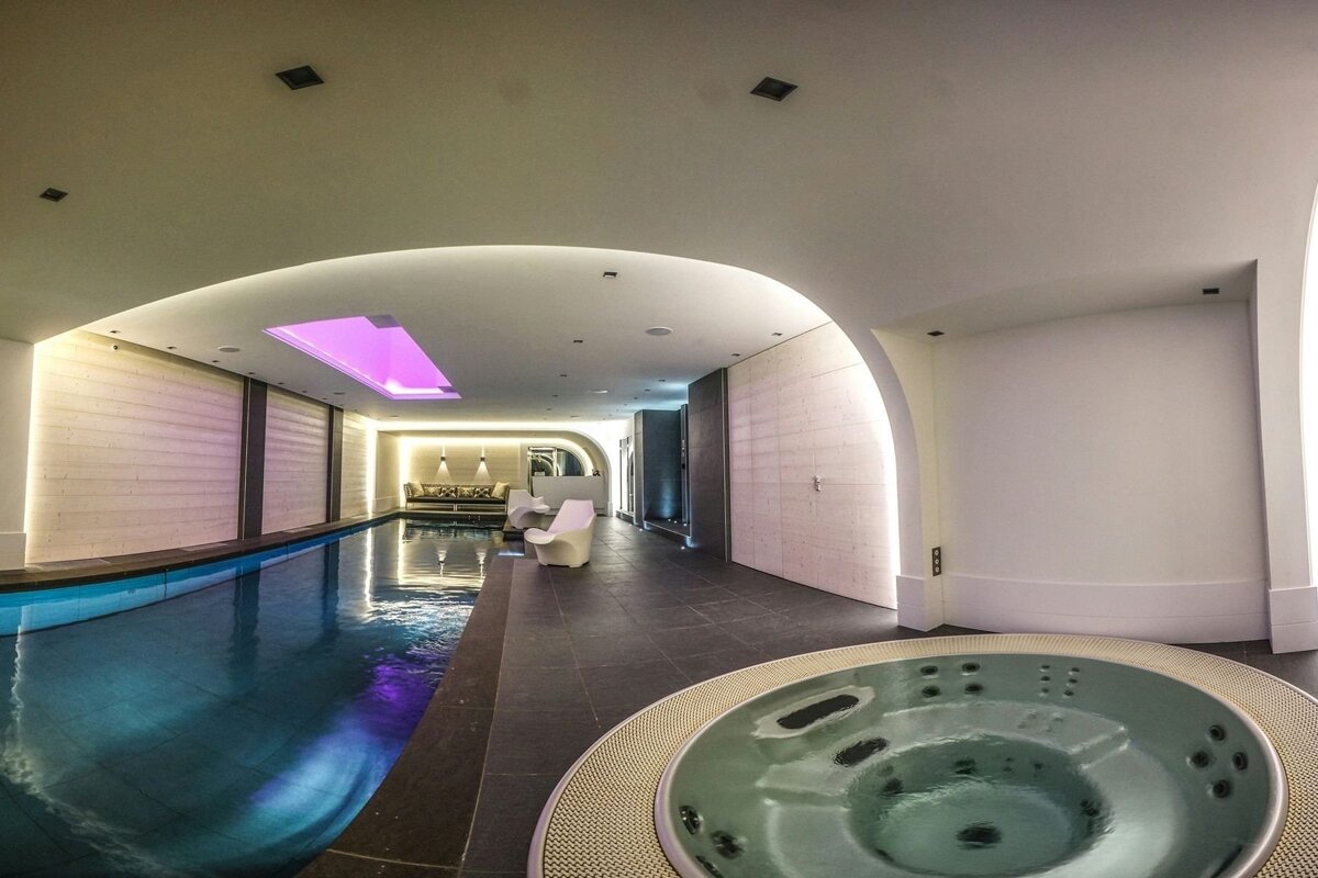 Modern indoor pool room featuring a jacuzzi, elegant ambient lighting, and a comfortable lounge area.