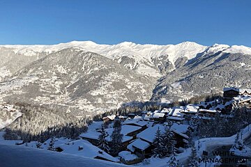 A breathtaking snowy mountain landscape features a village with snow-covered roofs under a clear blue sky, ideal for winter sports.