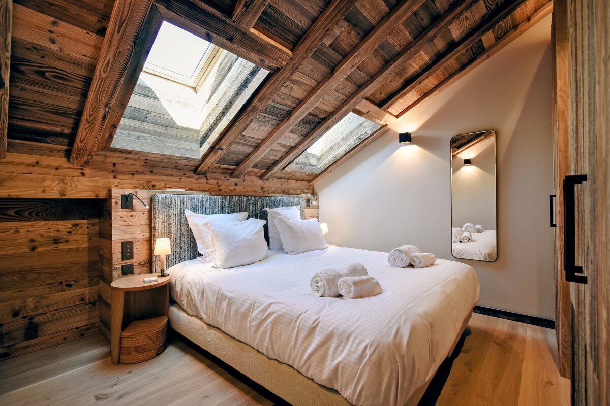 Cozy, wood-paneled attic bedroom with a bed, white linens, and bright skylights, creating a warm and inviting modern chalet feel.