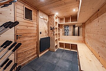 A wood-paneled ski room with benches, shelving, ski storage racks, and dark tile flooring.