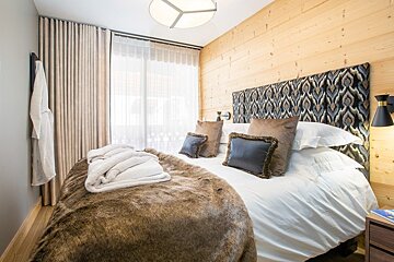 A cozy bedroom featuring a wood-paneled wall, patterned headboard, and a bed styled with a brown faux fur throw and plush pillows.