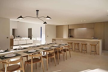 A sleek, modern open-concept dining room and kitchen with a long wooden table, island bar stools, and a light-colored aesthetic.