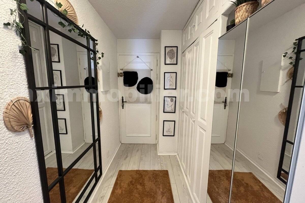 A modern hallway with light wood floors, a large black-framed mirror, white built-in wardrobes, brown rugs, and minimalist line art.