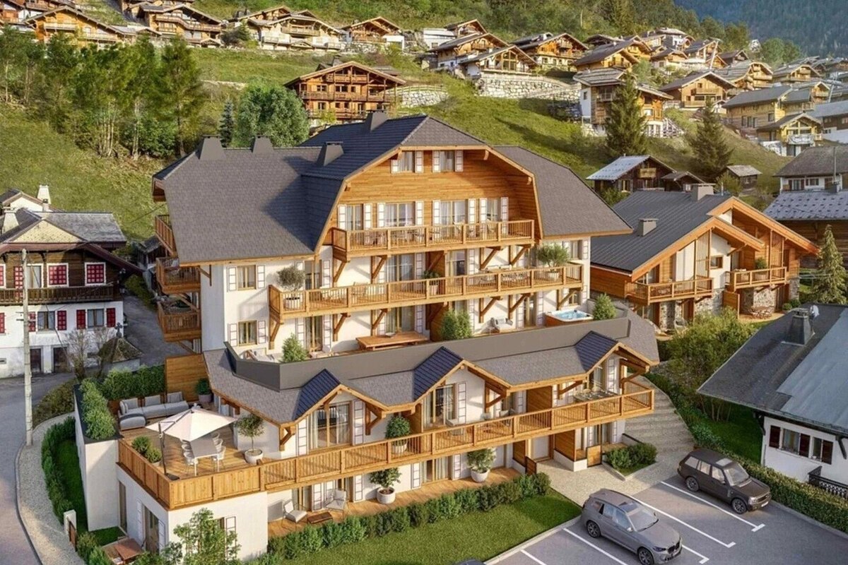 A large, modern multi-story alpine chalet building surrounded by traditional wooden houses on a scenic hillside village.