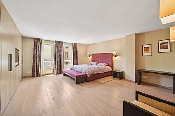 Large, contemporary bedroom with light wooden floors, a pink bed with a high headboard, built-in wardrobe, and windows.