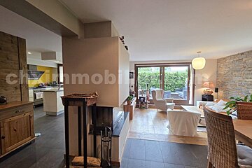 An open-plan home featuring a central fireplace, modern kitchen with a yellow wall, living/dining area with a stone accent wall, and glass doors leading to a patio.