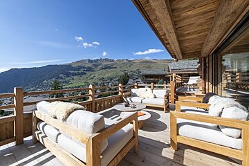A wooden deck with a couch and chairs and mountains in the background