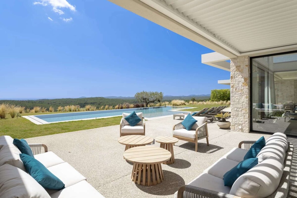 A chic outdoor patio with comfy seating, an infinity pool, and a vast, green landscape under a bright blue sky.