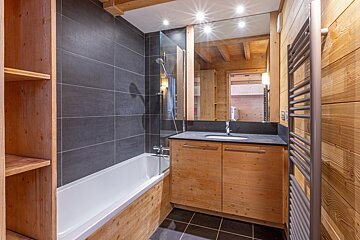 Modern bathroom with wood paneling, dark grey tiled walls/floor, a bathtub with shower, vanity, large mirror, and towel warmer.