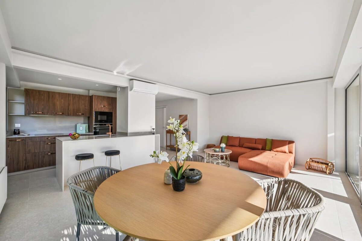 Bright, modern open-plan living area with an orange sofa, round dining table, and a stylish kitchen with dark wood cabinets and an island.
