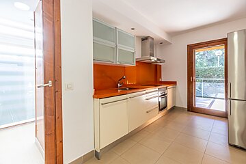 Bright, modern kitchen with orange counters & backsplash, cream cabinets, stainless steel appliances, tiled floor, and doors to outdoor spaces.