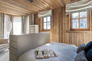 Cozy rustic bedroom with wood paneling, a fluffy bed with a tea tray, and windows revealing a glimpse of the outdoors.