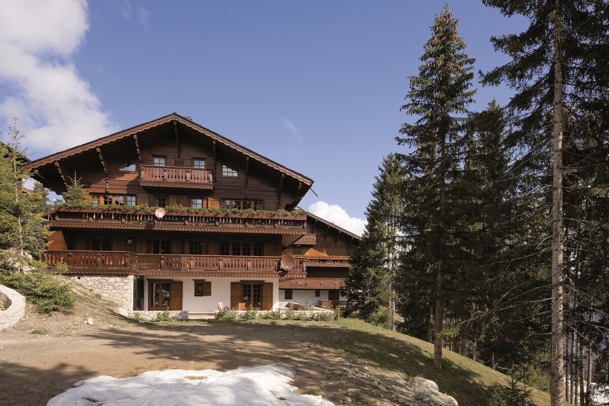 A large wooden house is surrounded by trees and snow