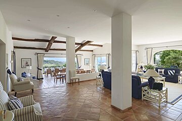 Spacious open-plan room with terracotta tiles, wood beams, distinct living & dining areas, and a panoramic view outside.