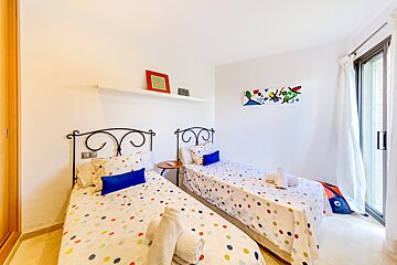 A bright bedroom features two twin beds with colorful polka dot bedding, wrought iron headboards, modern abstract art, and a sliding glass door.