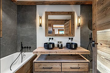 Rustic modern bathroom featuring a wooden double vanity with black vessel sinks, a matching framed mirror, slate wall tiles, and a bathtub.