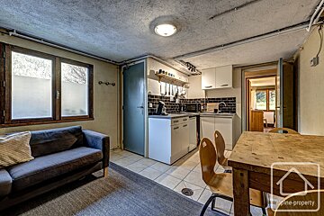 A rustic apartment kitchen and living area, featuring a couch, wooden dining set, and a small kitchenette.